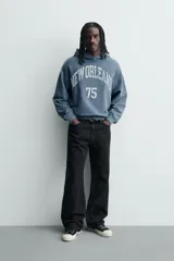 Sudadera tipo hoodie de corte relajado en color azul con efecto lavado. Presenta capucha, mangas largas, puños y ruedo en rib, con estampado frontal en color blanco con texto y números.