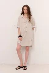 Vestido corto tipo camisa polo de lino en color beige, con mangas cortas abuchonadas con lazos en los puños, cuello camisero y cartera de botones frontal.