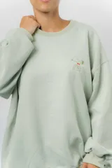 Buzo oversize de algodón frizado color beige, con cuello redondo, puños y cintura tejidos. Presenta un bordado pequeño de Snoopy en el frente.
