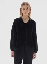 Camisa de terciopelo color negro, con cuello clásico, cierre frontal oculto y mangas largas con puños elásticos. Presenta un diseño holgado con cordón ajustable en el ruedo.