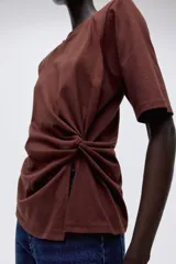 Remera de punto suave de algodón, color marrón, con cuello redondo, mangas cortas y detalle girado en un lateral que crea un efecto drapeado.