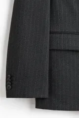 Blazer cruzado de tejido gris oscuro con finas rayas verticales blancas (pinstripe). Presenta solapas de pico, cierre de doble botonadura con botones oscuros, bolsillo superior insertado y dos bolsillos delanteros ribeteados con solapa. Tiene botones decorativos en los puños y abertura trasera.