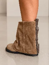Bota corta de cuero gamuzado color marrón, con diseño de polaina superpuesta y detalle de hebillas metálicas en la parte posterior del talón. Cuenta con suela plana de goma negra y horma amplia.