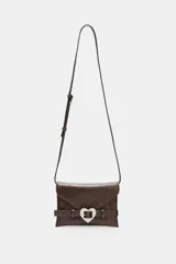 Bolso tipo bandolera de cuero sintético color marrón oscuro, con solapa frontal y cierre de botón imantado. Presenta un cinturón decorativo con hebilla metálica en forma de corazón plateado. Incluye asa larga ajustable y bolsillo interior con cierre.