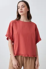 Blusa blanca de corte holgado con cuello redondo, mangas cortas con detalle de volados y ruedo con terminación de volado pequeño.