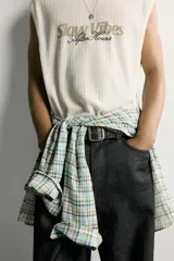 Camiseta tank blanca de corte relajado, con textura en relieve, cuello redondo y sisas amplias. Cuenta con un diseño bordado y estampado en el centro del pecho con las inscripciones "Slow Vibes" y "After Hours" en tonos verde y negro.