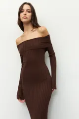 Vestido largo de punto acanalado en color negro, con diseño de hombros descubiertos y mangas largas. Presenta un corte ajustado al cuerpo y aberturas laterales en el ruedo.