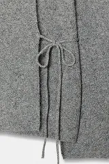 Chaqueta de punto gris con cuello redondo, manga larga acampanada y cierre frontal cruzado con botón y lazada lateral.