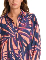 Camisa de gasa con estampado de hojas en tonos azul y coral, con cuello camisero, cierre frontal de botones y mangas tres cuartos con puños fruncidos.