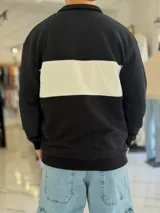 Hoodie de corte clásico con medio cierre y cuello alto, en color marrón con una franja horizontal blanca en el pecho que incluye el logo estampado en negro. Presenta además un pequeño bordado en el hombro izquierdo y puños y cintura elastizados de rib.