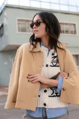 Chaqueta corta tipo blazer color marrón, confeccionada en tela de lana afieltrada. Tiene cuello camisero, silueta cuadrada, cierre frontal con botones y bolsillos delanteros.