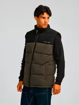 Chaleco acolchado bicolor con diseño de bloques en negro y verde oliva. Presenta cierre frontal completo, cuello alto, bolsillos laterales con cierre y logo de la marca estampado en el pecho.