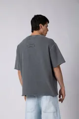 Remeron de corte oversized con cuello redondo y mangas cortas. Presenta un acabado de tela con efecto desgastado y costuras visibles en los bordes, con una etiqueta pequeña en el lateral inferior.