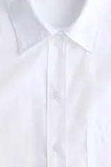 Camisa blanca oversized de manga larga, con cuello clásico, cierre frontal de botones, un bolsillo aplicado en el pecho y dobladillo redondeado.