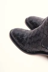 Bota tipo botineta de cuero negro con diseño trenzado artesanal en toda la capellada. Presenta paneles laterales elásticos, taco cuadrado de altura media y tirador en la parte superior trasera.