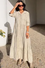 Vestido largo de estilo camisero en color azul, con cuello clásico, cierre frontal de botones y mangas tres cuartos con trabillas. Presenta un diseño de falda con cortes horizontales que le otorgan volumen y movimiento.
