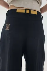 Pantalón de lino marrón de tiro medio, con calce holgado y diseño de piernas amplias. Cuenta con bolsillos traseros, trabillas para cinto y un pin bordado en contraste.
