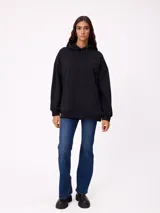 Canguro negro de corte holgado con capucha y cordones ajustables. Presenta un bolsillo frontal tipo canguro y un pequeño logo bordado en el pecho.