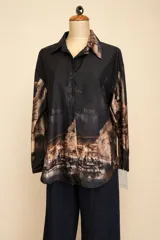 Camisa de seda con estampado artístico de escenas parisinas en tonos marrones sobre fondo negro, de corte holgado, cuello clásico y cierre frontal con botones.