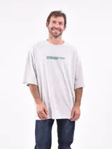 Remera de manga corta color gris claro, corte oversize, con cuello redondo y un pequeño estampado en el pecho con texto en color verde.