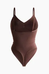 Body tanga de color marrón oscuro, con efecto vientre plano y copas forradas sin aros con sección en punto menguado para realzar el busto. Posee breteles ajustables y refuerzo interior con botones a presión ocultos.