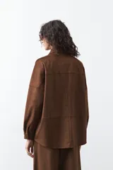 Sobrecamisa de gamuza color marrón, de silueta relajada, con cuello camisero, botones frontales y bolsillos de parche en el pecho.