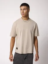 Remera de manga corta color gris piedra, de corte oversize y cuello redondo, con pequeño parche bordado en el dobladillo inferior.