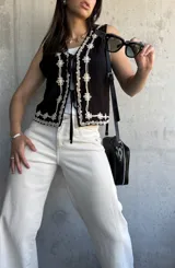 Chaleco negro con bordado de flores blancas, escote en V y lazos de ajuste en el frente.