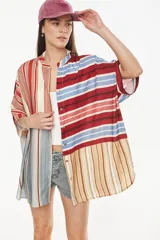 Vestido camisero corto con diseño de paneles combinados en distintos patrones de rayas verticales y horizontales, en tonos rojo, azul, beige y blanco. Posee cuello mao, cierre frontal con botones y mangas cortas caídas.