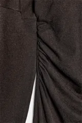 Vestido midi de punto color marrón, con cuello subido, manga larga y diseño cut out en un hombro. Presenta frunces laterales en la cintura que aportan un efecto drapeado.