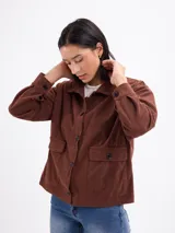 Campera de pana color beige, con cuello camisero, cierre frontal de botones oscuros, mangas largas con puños abotonados y dos bolsillos frontales con solapa.