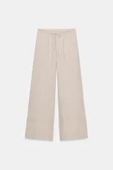 Pantalón palazzo de tiro alto, color beige claro, confeccionado en lino 100%. Presenta cintura ajustable con cordones anudados al frente y pierna ancha.