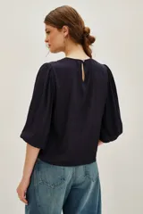 Camisa de color azul marino con mangas tres cuartos abullonadas y puños elásticos. Presenta un diseño con paneles de encaje negro en el frente y cuello redondo.