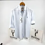 Camisa de manga larga a rayas verticales celestes y blancas, con cuello abotonado y logo bordado en el pecho. Marca Duxon.