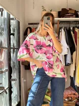 Blusa blanca de corte holgado con diseño estampado de flores grandes en tonos fucsia y hojas verdes, escote redondo y mangas cortas amplias.