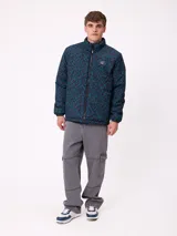 Campera reversible de nylon con cuello alto y cierre frontal. Un lado es de color gris liso con logo bordado, mientras que el otro lado presenta un estampado abstracto en tonos azules. Cuenta con bolsillos laterales y puños elásticos.