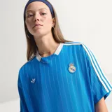 Camiseta de fútbol Adidas del Real Madrid, inspirada en los años 80. Diseño de color azul con finas rayas verticales blancas, cuello en V blanco, mangas cortas con las tres tiras características de la marca y escudo retro del club bordado en el pecho.