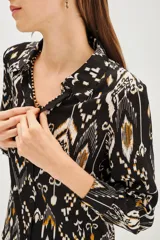 Camisa de manga larga con cuello camisero y cierre frontal de botones. Presenta un estampado étnico tipo ikat en tonos negro, blanco y ocre.