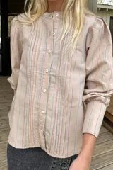 Camisa de manga larga con diseño a rayas verticales en tonos beige, lila y turquesa. Presenta cuello redondo, cierre frontal con botones y detalles de alforzas verticales en el frente. Las mangas tienen frunces en los hombros y puños anchos.
