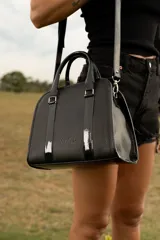Cartera tipo bowling de cuero vacuno color negro, con doble asa corta y correa larga extraíble. Tiene cierre metálico YKK, bolsillo interno con cierre y logo de la marca grabado en el frente.