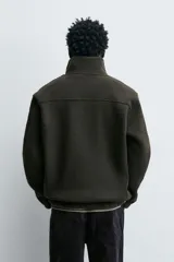 Sudadera de corte relajado confeccionada en tejido con textura. Presenta cuello subido con cierre frontal de cremallera metálica y manga larga.