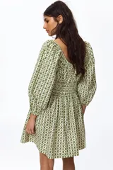 Vestido corto de algodón con estampado geométrico en tonos verdes y blancos. Cuenta con escote en V, mangas globo con elástico en los puños, cuerpo fruncido tipo nido de abeja en la cintura y falda con vuelo.
