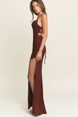 Vestido largo de fiesta confeccionado en tela lurex color bordó. Presenta un escote recto con breteles finos, corte ajustado al cuerpo y una abertura lateral profunda en la falda.