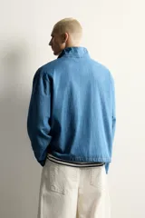 Camisa polo de corte relajado confeccionada en denim ligero de algodón con efecto lavado. Presenta cuello subido, cierre frontal con botonadura oculta por solapa, manga larga, bolsillo de plastrón en el pecho y bajo ajustable con cordón.