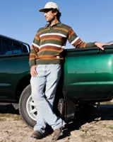 Buzo tejido de punto con diseño de rayas horizontales en tonos verde, marrón y blanco. Presenta cuello tipo polo con cierre de tres botones, mangas largas con puños acanalados y logo de la marca bordado en el pecho. Incluye una etiqueta decorativa en la parte inferior.