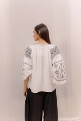 Blusa blanca con bordados en contraste de estilo bohemio, mangas amplias y diseño ligero.