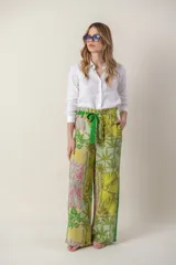 Pantalón ancho con estampado de hojas y flores en tonos verdes, amarillos y rosados. Tiene cintura alta con lazo verde.
