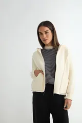 Abrigo negro con capucha, confeccionado en tejido de textura suave. Presenta cierre frontal con cremallera, bolsillos laterales integrados con costuras decorativas y puños ajustados.