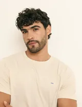 Remera básica de algodón color beige, de manga corta, con cuello redondo y un pequeño detalle bordado en el pecho.