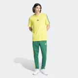 Remera Adidas de algodón color amarillo, con cuello redondo y mangas cortas. Presenta el logo de la marca bordado en el centro del pecho y las icónicas tres rayas de la marca en color verde sobre los hombros y mangas.